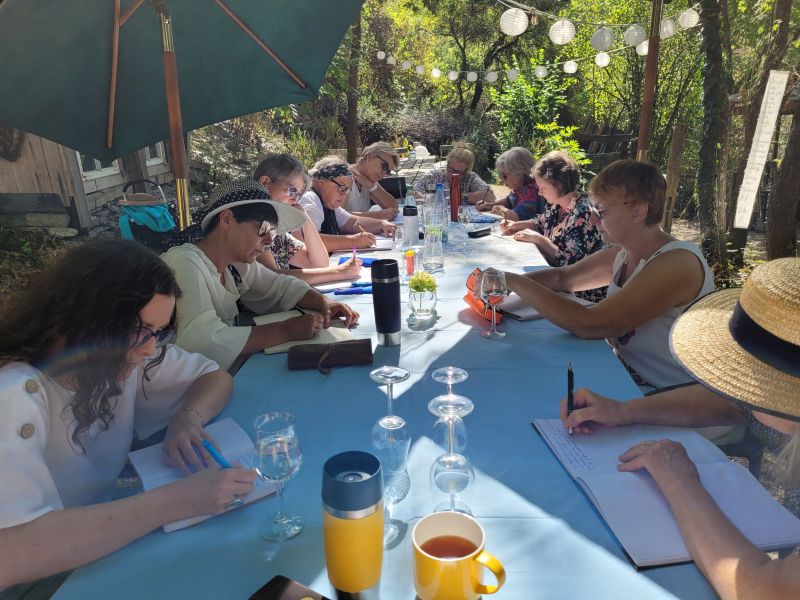 Ein langer Tisch im Freien an dem zehn schreibende Frauen sitzen.