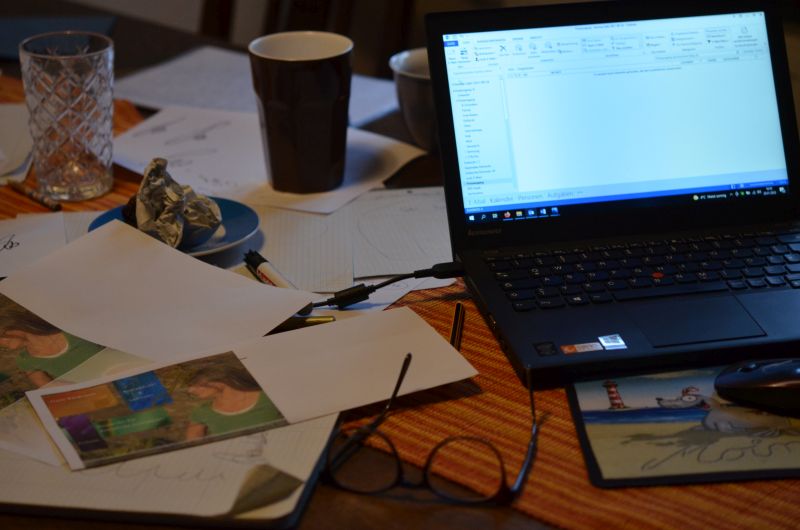 Ein unaufgeräumter Schreibtisch mit vielen Zetteln, Stiften und Trinkgefäßen samt aufgeklapptem Laptop:
Arbeitstisch einer Ideen-Entwicklung für die eigene Website