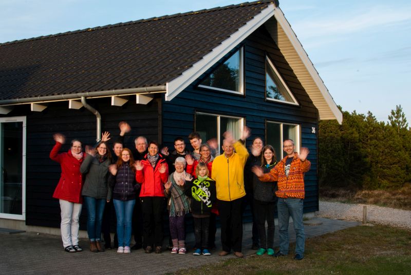 Ein Ferienhaus in Blavand/Dänemark, davor eine fünfzehnköpfige, winkende Familie mit drei Generationen