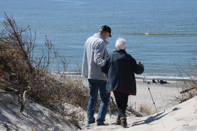 Zwei Personen gehen eine Düne an Dänemarks Nordseeküste hinunter, die ältere Dame wird dabei von ihrem Sohn unterstützt.