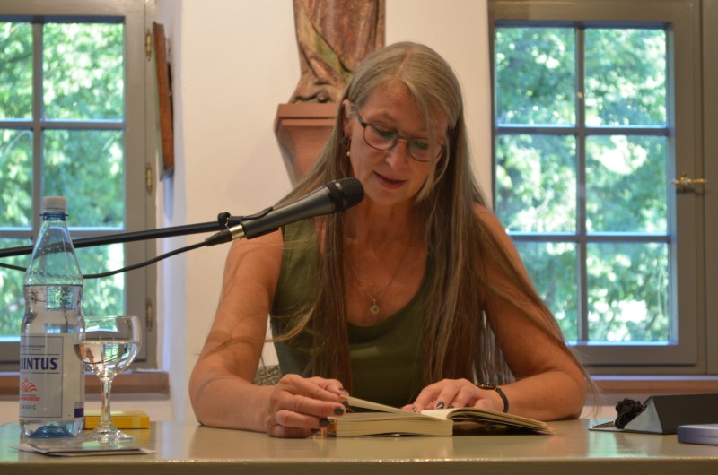 Eine Autorin sitzt an einem Tisch und liest aus einem Buch vor.
