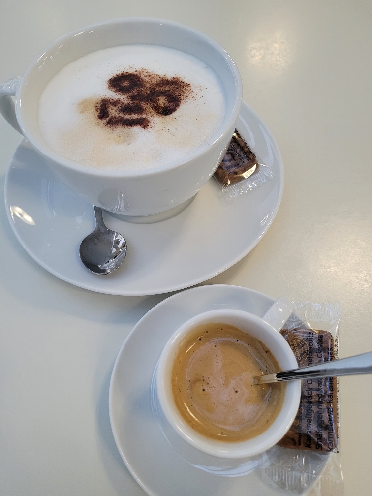 Ein Cappucino mit Kakao-Smily und eine Tasse Espresso