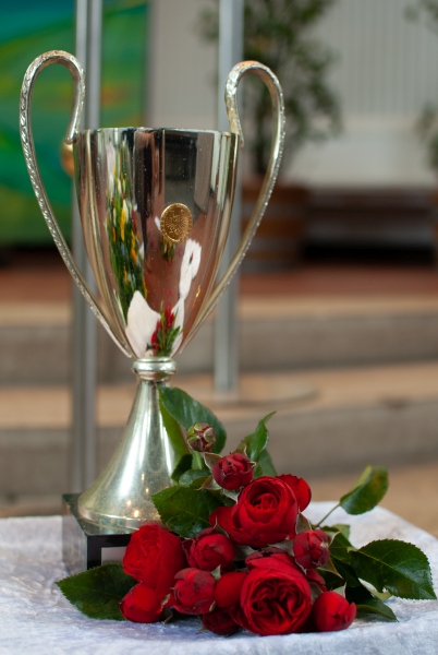Ein silberner Pokal mit roten Rosen dekoriert.