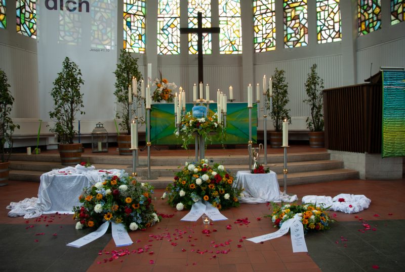 Der Altarraum in einer evangelischen Kirche, im Vordergrund Kränze mit Urne