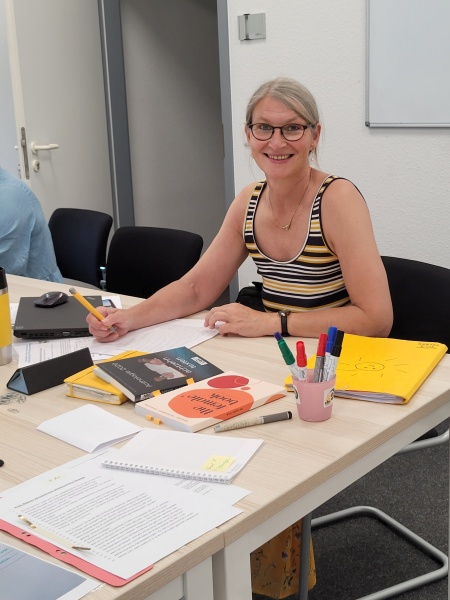 Frau in einem Seminarraum umgeben von Büchern und Schreibutensilien