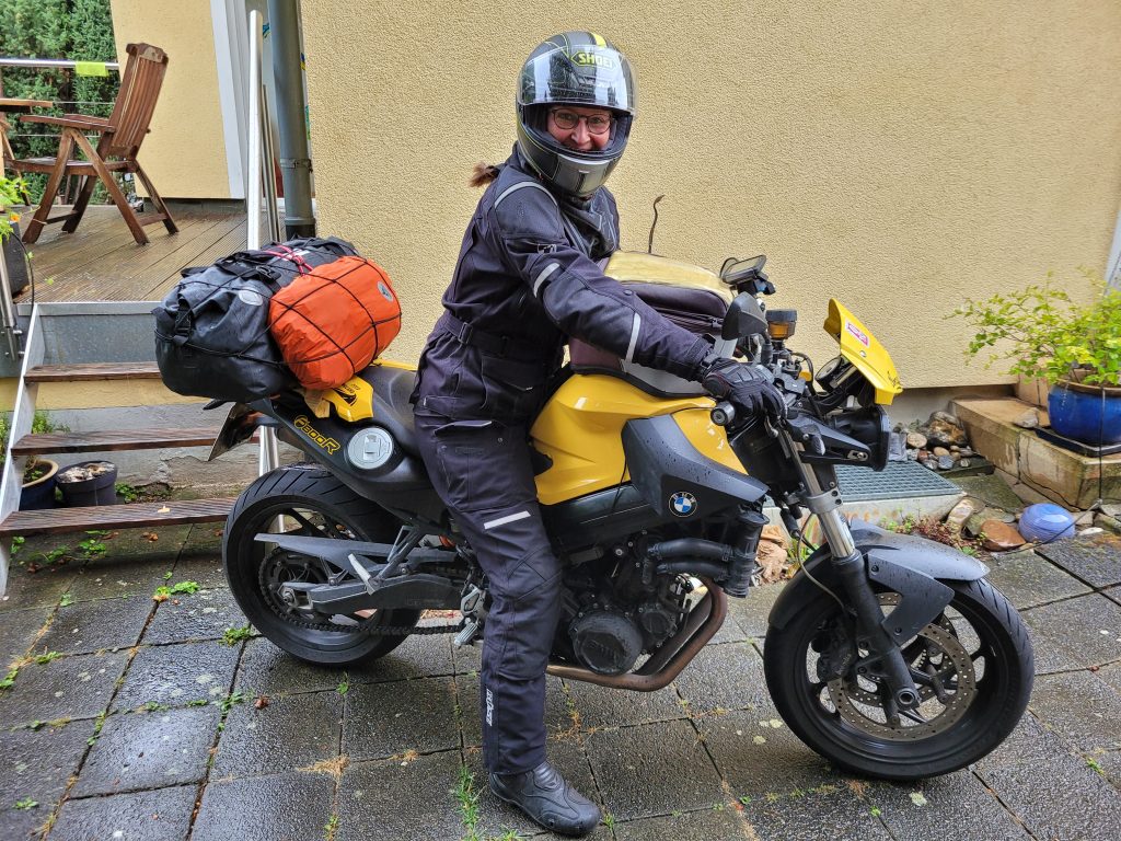 Frau in Regenkombi auf bepacktem Motorrad, einer BMW F800R in schwarz-gelb.