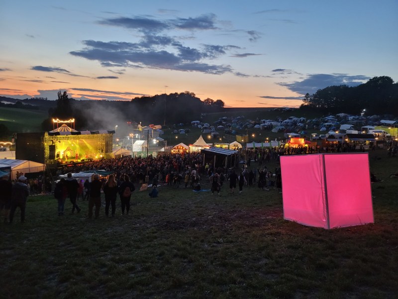 Abendstimmung auf dem Gelände des Lott-Festivals mit Bühne und Publikum, rechts im Vordergrund der leuchtende Cubus.