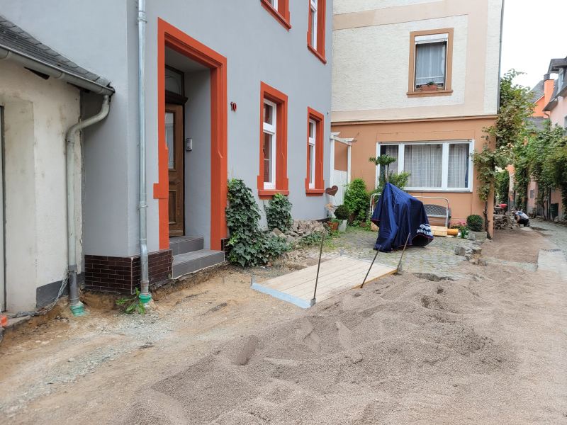 Hausfront in einer Straßenbaustelle, ein Motorrad steht unter einer Plane davor.