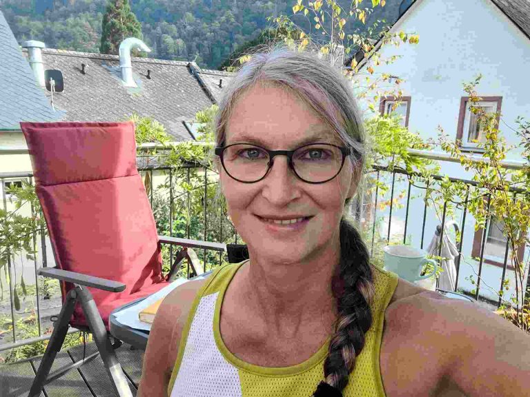 Frau mit geflochtenem Zopf auf Balkon lächelt in die Kamera