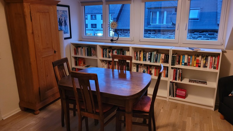 Bücherregale, ein Schrank und ein Tisch vor einer Fensterfront