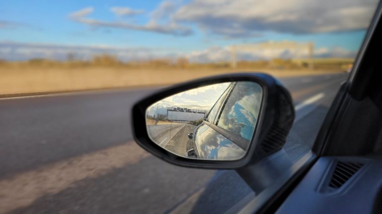 Blick in einen Seitenspiegel auf der Autobahn bei blauem Himmel mit wenigen Wolken