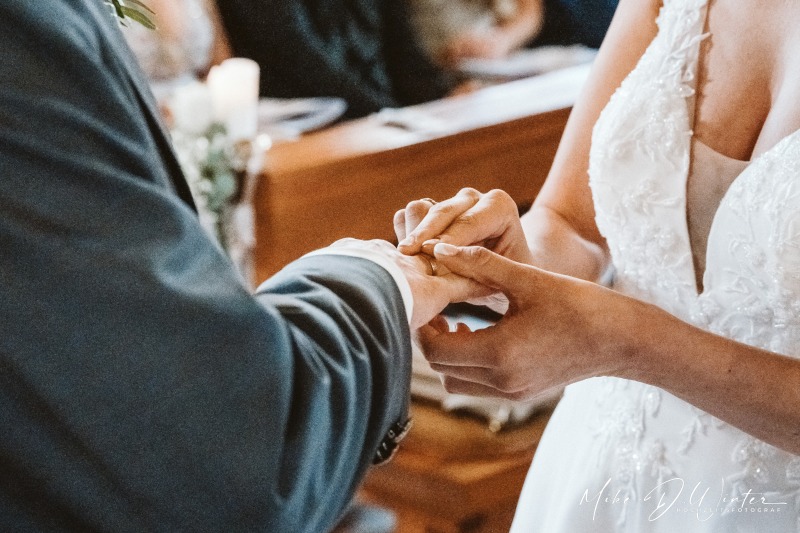 Die Braut steckt ihrem Bräutigam den Ring an den Finger.