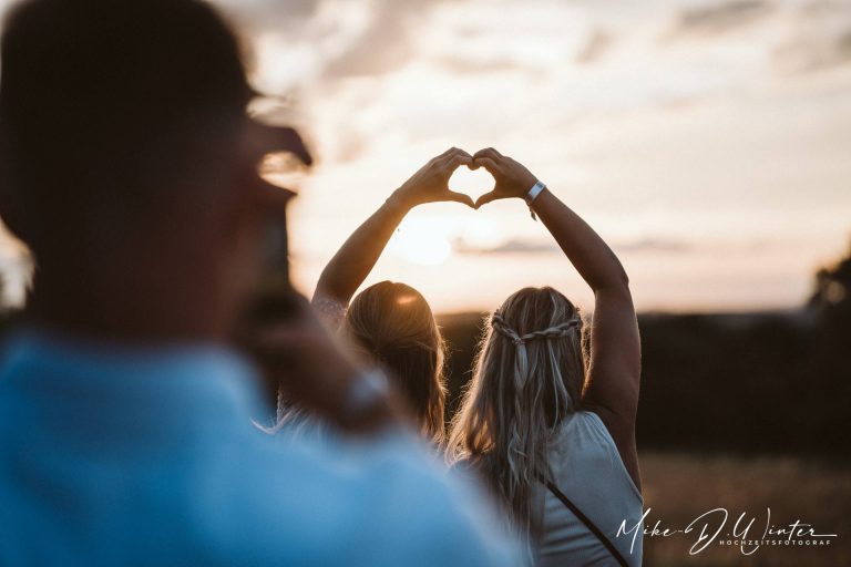 Brautleute werden bei Sonnenuntergang fotografiert, dabei bilden ihre Hände ein Herz