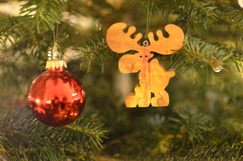 Eine rote Weihnachtsbaumkugel und ein Holz-Elch hängen am Baum.