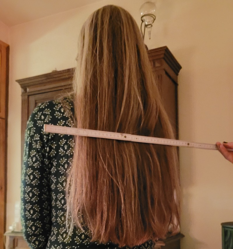 Die Rückansicht einer Frau mit ca. 70 cm langen Haaren, ein Zollstock zeigt die Länge von 35 cm an.