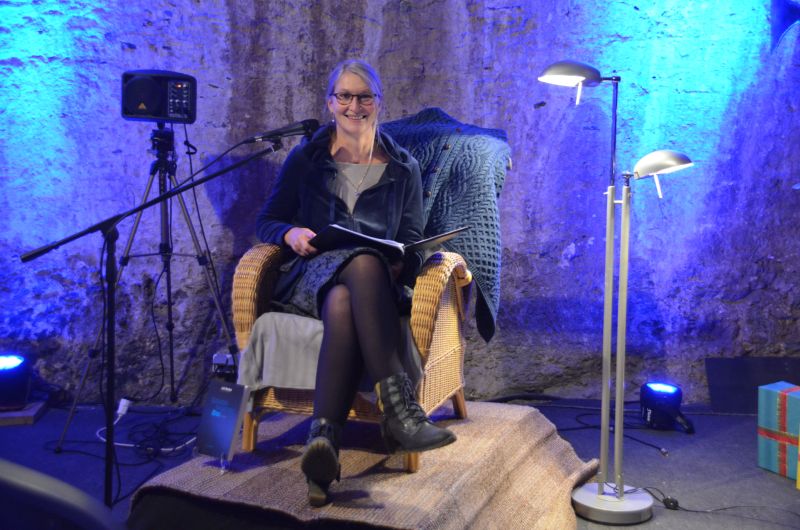 Die Autorin Juli Norden sitzt lächeln in ihrem Lesesessel vor einer blau illuminierten Wand.