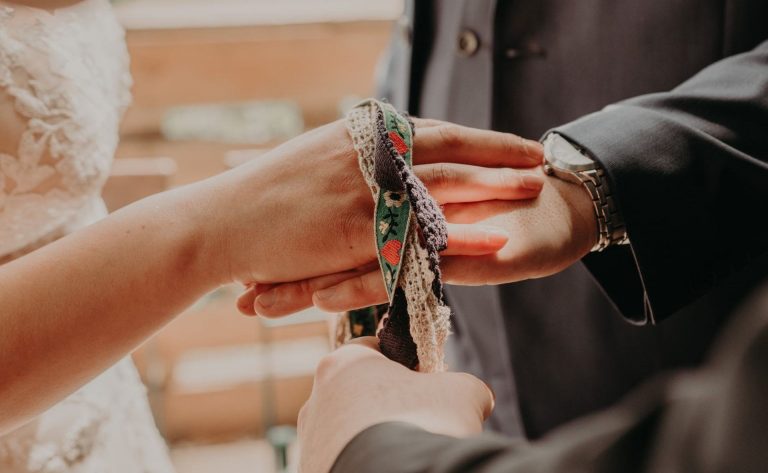 Auf den Händen eines Brautpaares liegt ein buntes Band fürs Handfasting