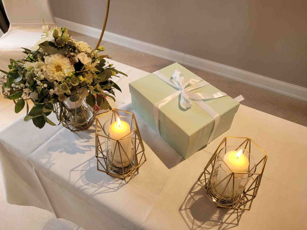 Tisch mit Blumenstrauß, Geschenkbox und zwei brennenden Kerzen