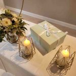 Tisch mit Blumenstrauß, Geschenkbox und zwei brennenden Kerzen