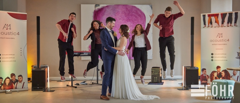 Brautpaar tanzt vor Liveband, zwei Musiker springen im Hintergrund in die Luft.