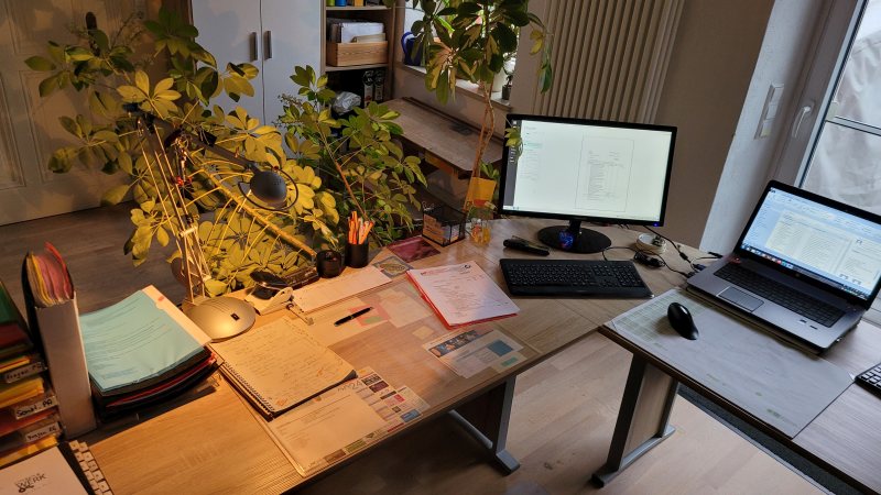 Schreibtisch mit Bildschirm, Laptop und Unterlagen