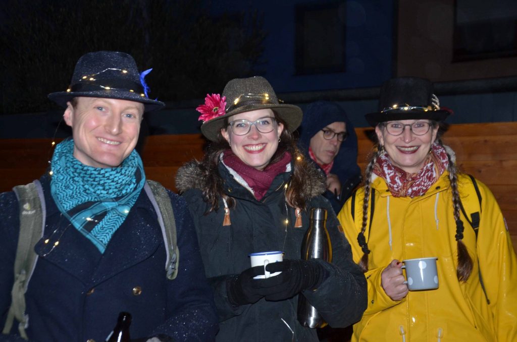 Drei fröhliche Menschen im Dunkeln beim Geisterzug in Köln mit Teebechern in der Hand