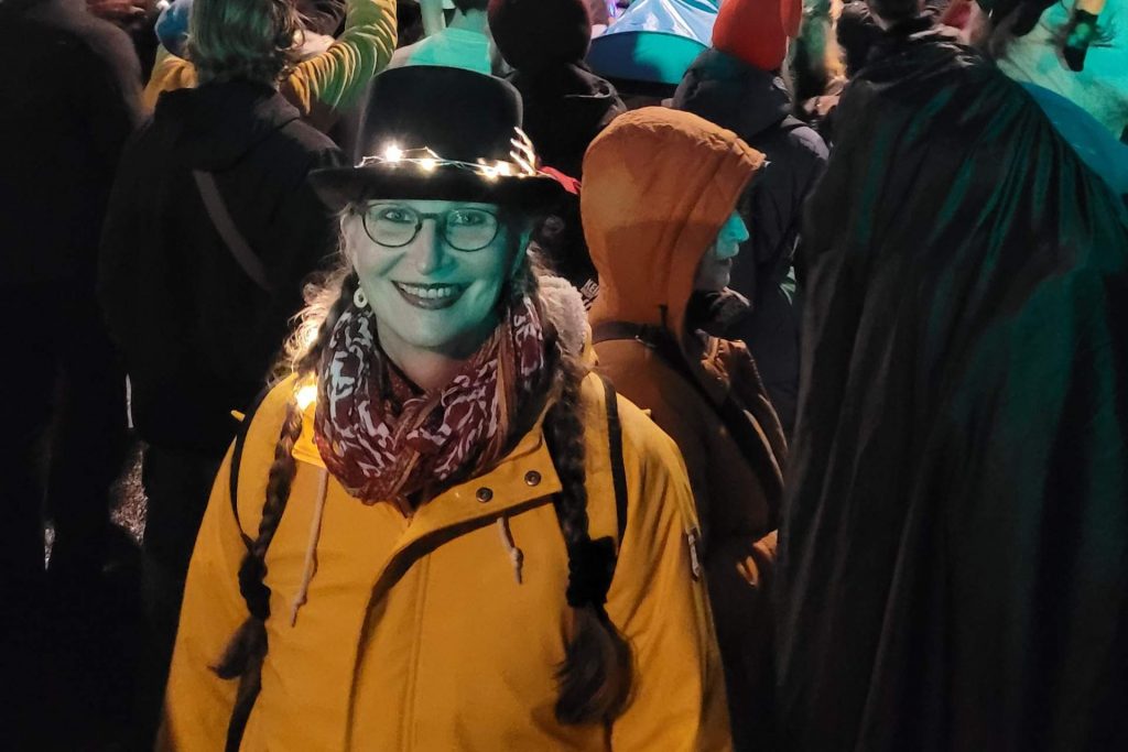 Frau mit Zylinder, der mit Lichtern illuminiert ist, in gelbem Mantel, lächelt in die Kamera
