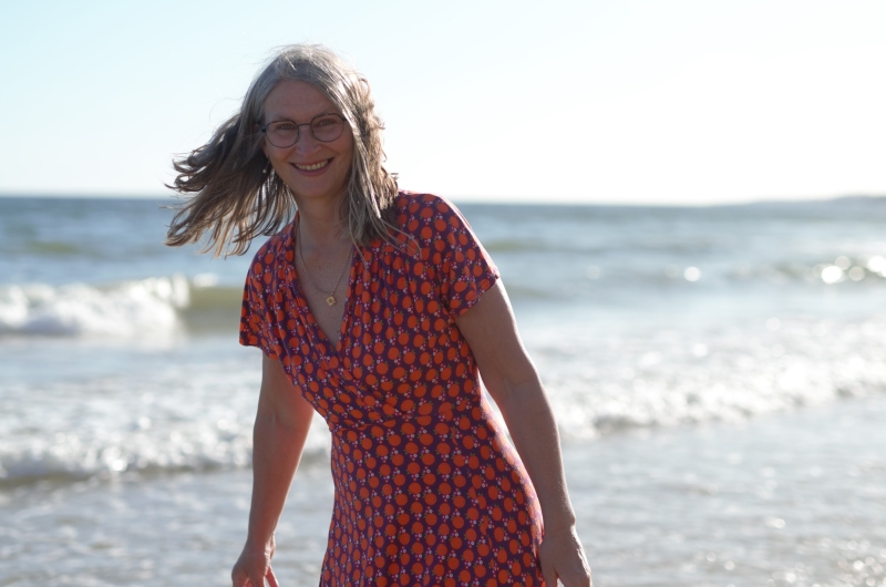 Frau am Strand vor der Brandung in rot-buntem Kleid und wehenden Haaren