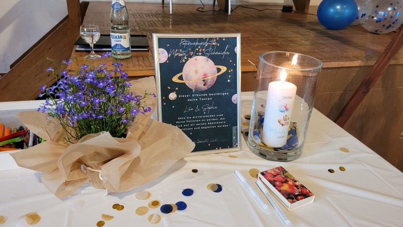 geschmückter Tisch mit Patenurkunde und brennender Taufkerze bei einem Kinderwillkommensfest