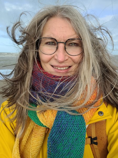 Frau mit vom Wind verwehten Haaren um buntem Schal am Meer