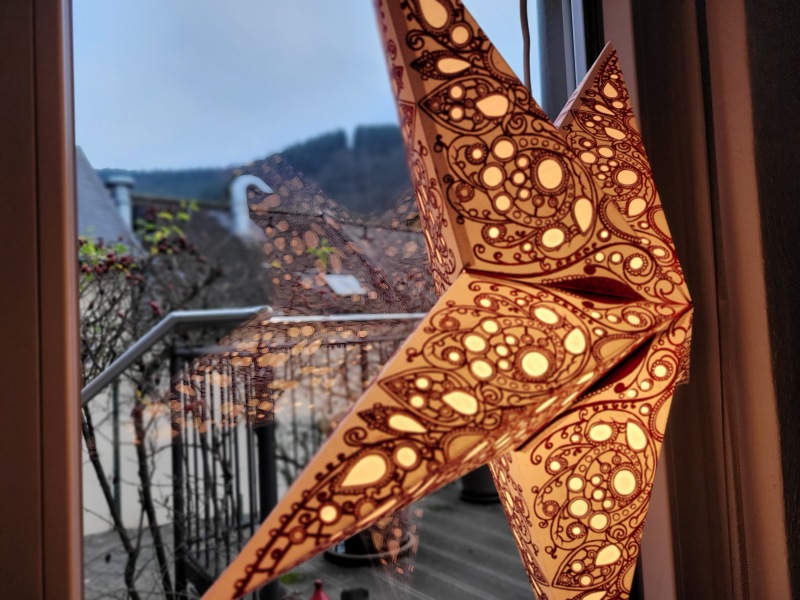 Rot-goldener Stern vor einem Fenster mit Blick auf die anbrechende Dämmerung