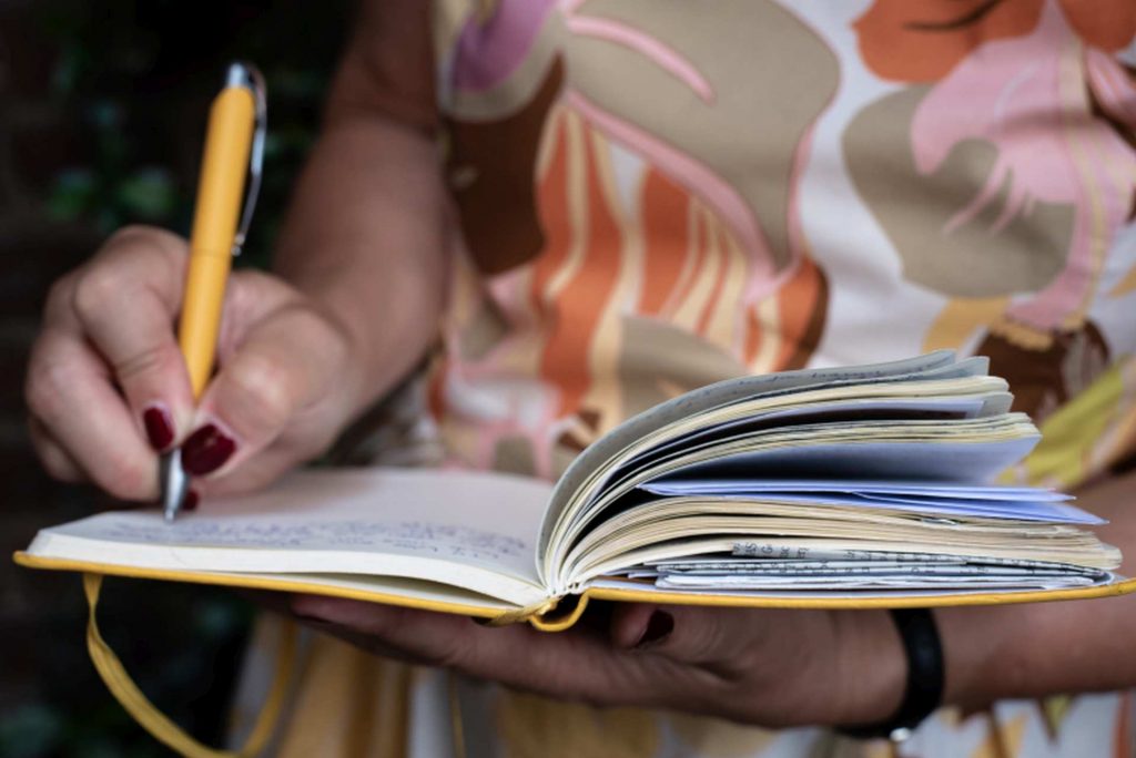 Schreibende Frauenhand in gelbem Notizbuch