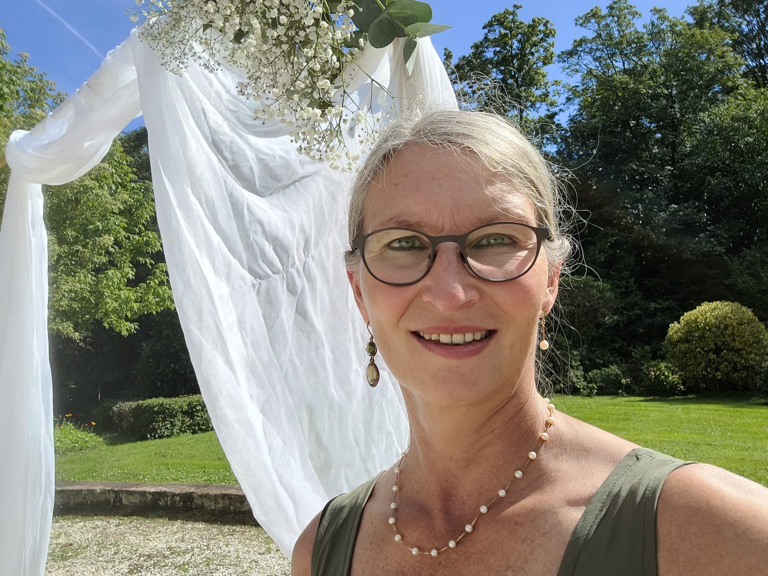 Frau mit Brille vor Traubogen lächelt in die Kamera