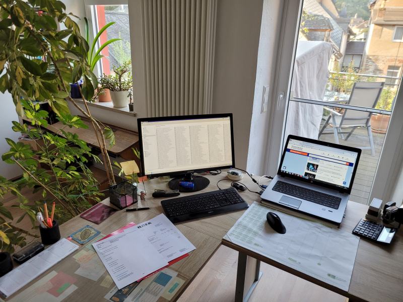Ein Eckschreibtisch mit Laptop und zweitem Bildschirm, auf dem Tisch Papiere