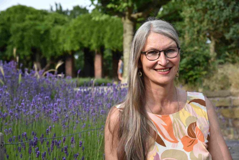 Lächelnde Frau mit langen Haaren und Brille vor blühendem Lavendel