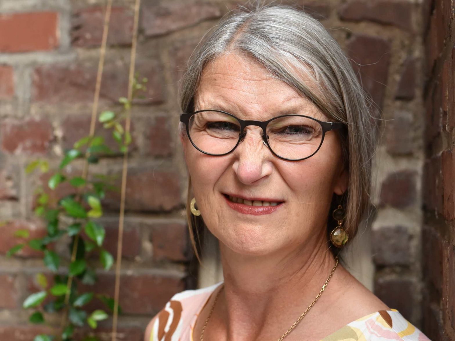 Frau mit langen grauen Haaren schaut skeptisch in die Kamera.