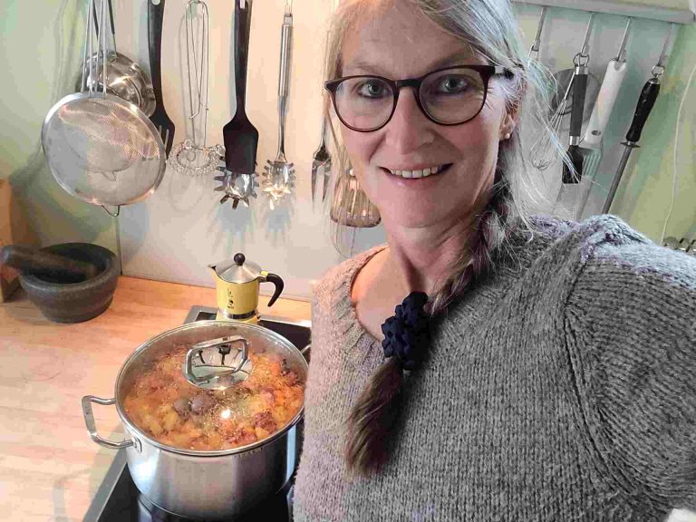 Frau in Küche lächelt in die Kamera, neben ihr Steckrübeneintopf auf dem Herd