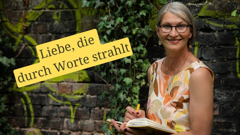 Lächelnde Frau vor Efeu-Wand mit einem Notizbuch in der Hand, darauf der Claim "Liebe, die durch Worte strahlt"