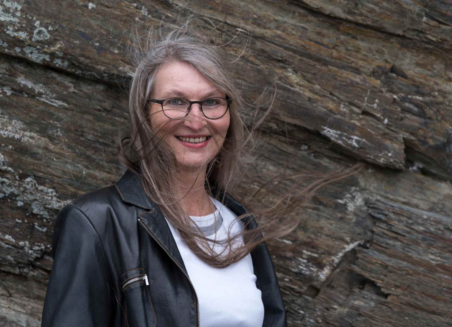 Frau vor Schiefermauer, deren lange Haare vom Wind verwirbelt werden