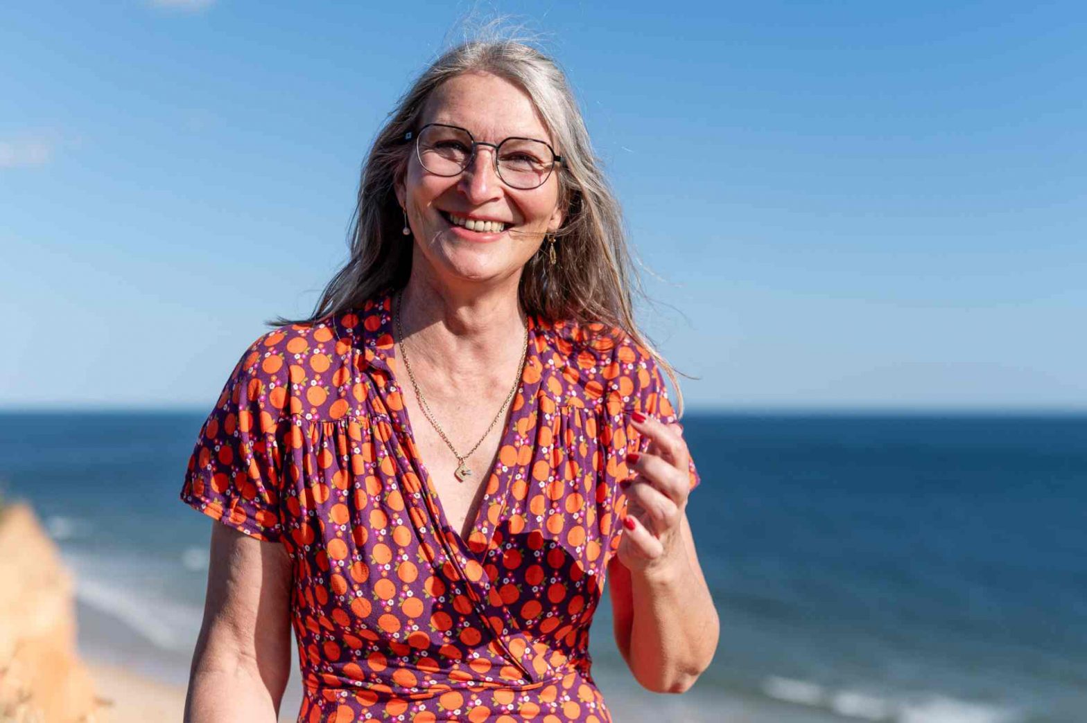 Frau in orange-buntem Klein am Meer lacht in die Kamera