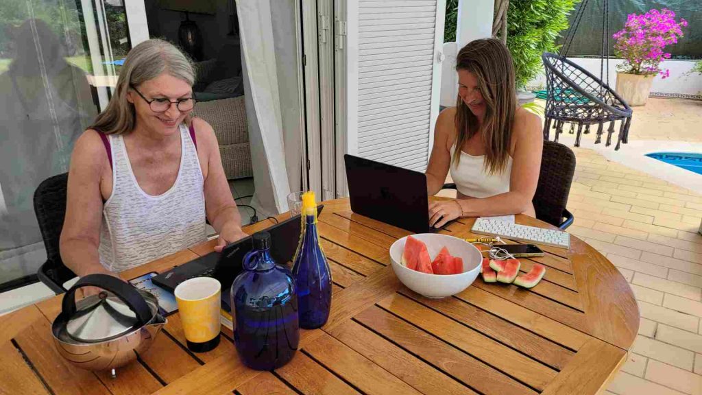 Zwei Frauen arbeiten auf einer Terrasse an ihren Laptops im Rahmen einer Workation.