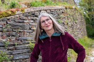 Frau vor Schieferbruchsteinwand schaut überlegend in den Himmel