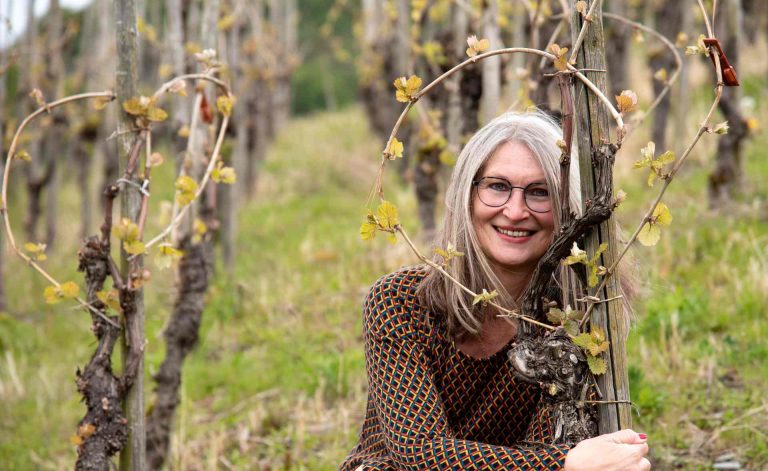 Frau kniet an einem Weinstock in den Moselweinbergen, die Stöcke sind in Herzform gebunden