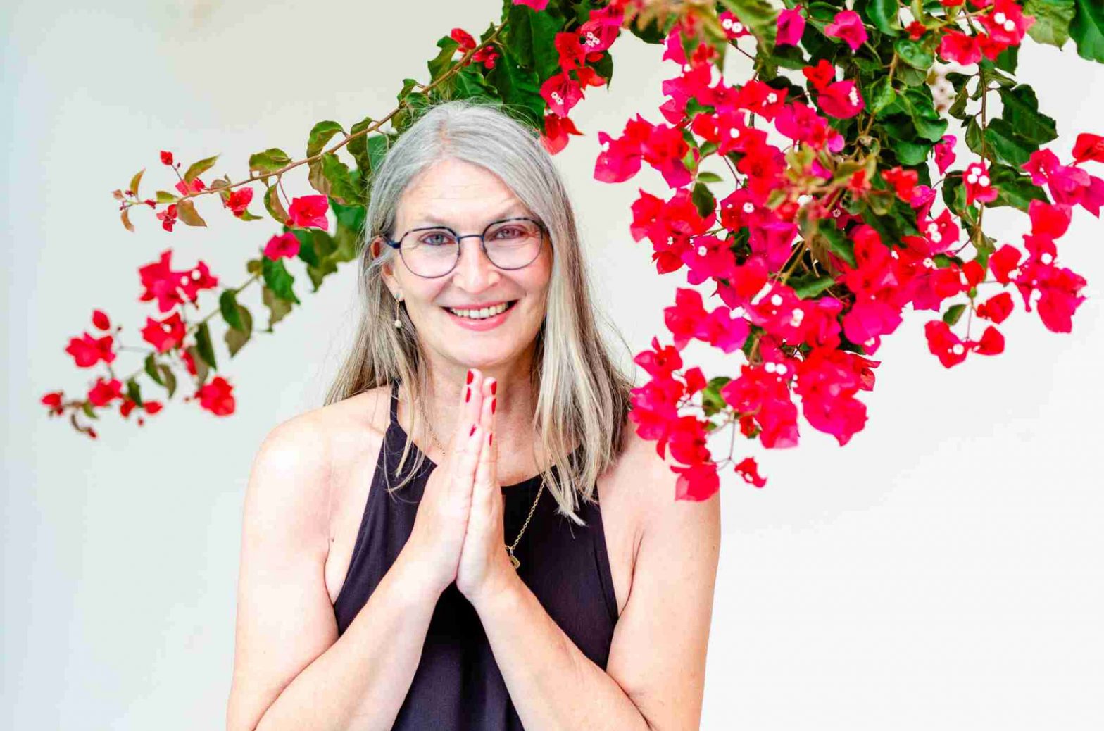 Frau im Sommerkleid vor heller Wand mit Bougainvillea und Danke-Handgeste