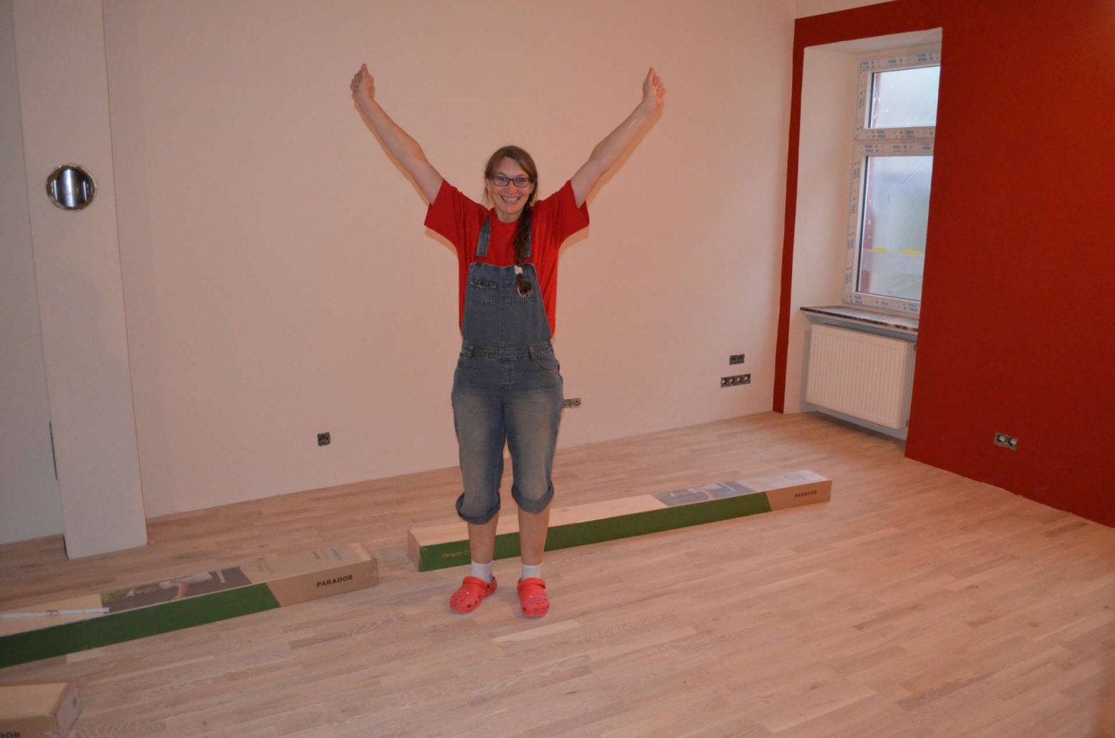 Frau steht jubelnd mit erhobenen Händen in Wohnzimmer, das renoviert wird