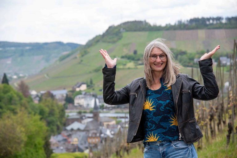 Frau mit nach oben geöffneten Armen und Händen vor Weinbergspanorama