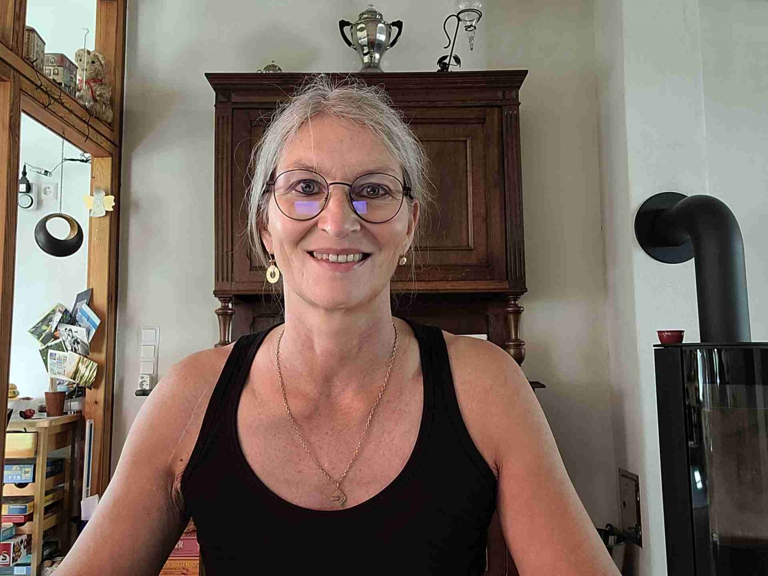 Frau schaut frontal in die Kamera, im Hintergrund ein altes Holzbufett