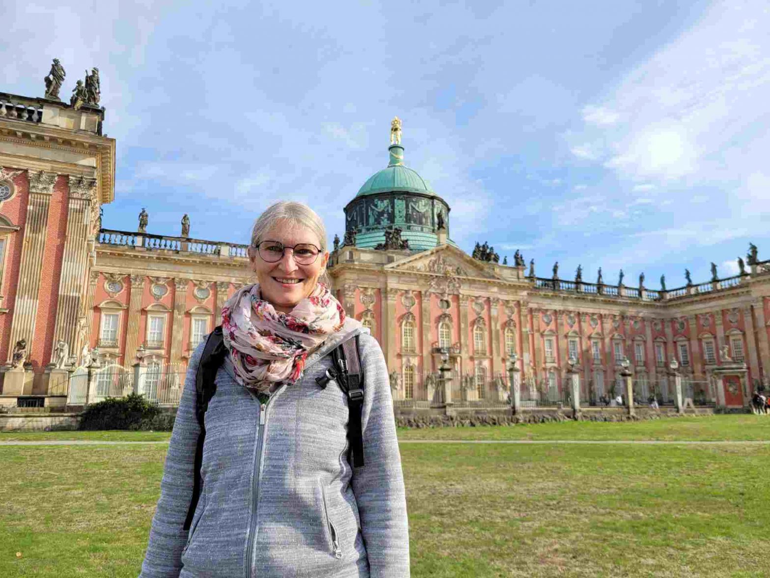 Frau steht vor dem Neuen Palais in Potsdam und lächelt in die Kamera