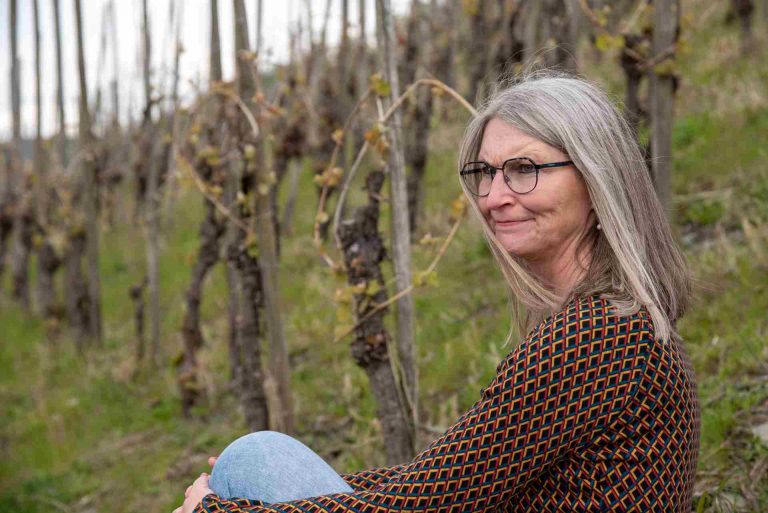 Frau mit skeptischem Blick sitzt in Weinbergen, seitliche Aufnahme