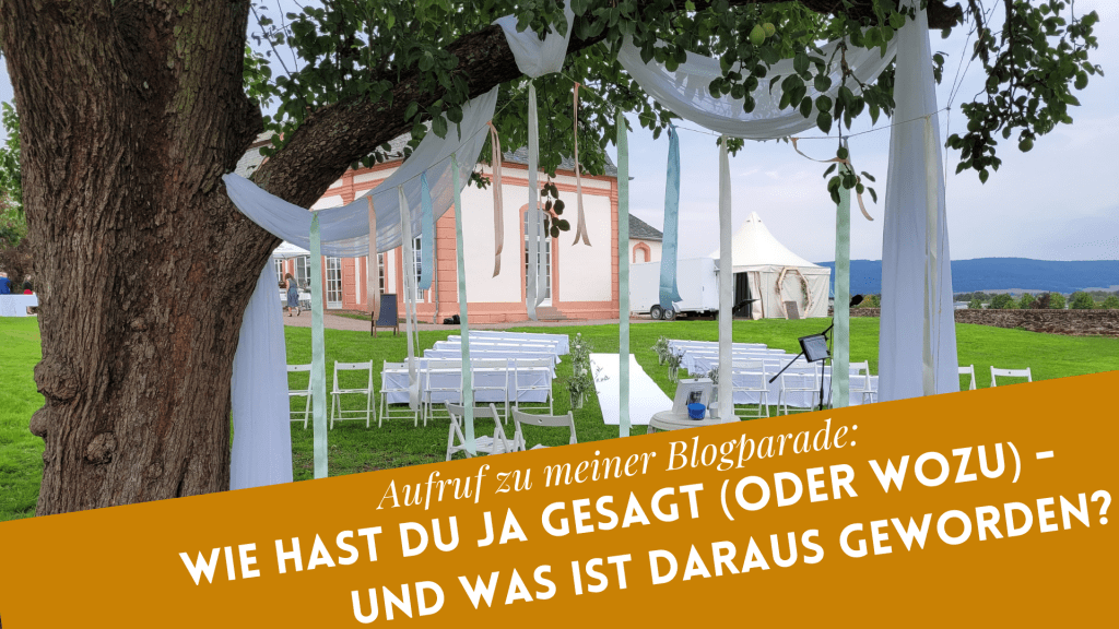 Freie Trauung draußen, weiße Stuhlreihen im Hintergrund, im Vordergrund ein Baum mit weißen Schals als Deko